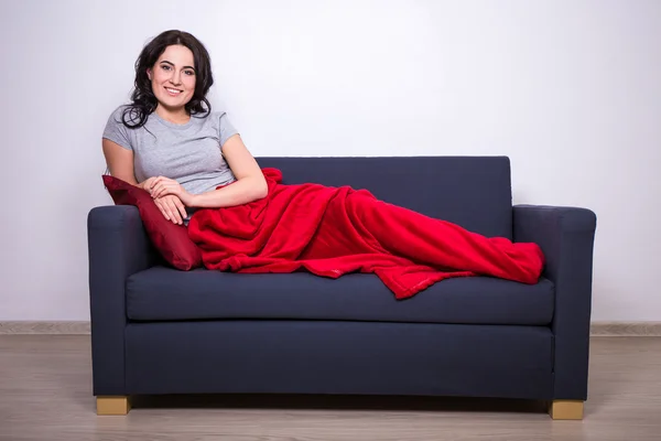 Jeune femme assise sur le canapé, enveloppé dans une couverture rouge — Photo