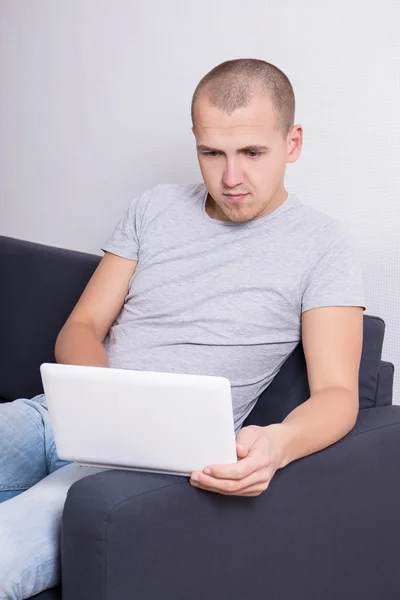 Pohledný muž sedí na pohovce s počítačem — Stock fotografie