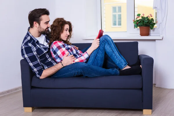 Livro de leitura feliz jovem casal no sofá — Fotografia de Stock