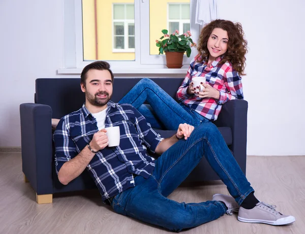 Ungt par sitter på soffan med koppar te eller kaffe i livin — Stockfoto