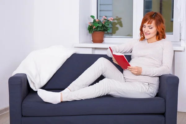 Mujer embarazada feliz lectura libro en la sala de estar — Foto de Stock