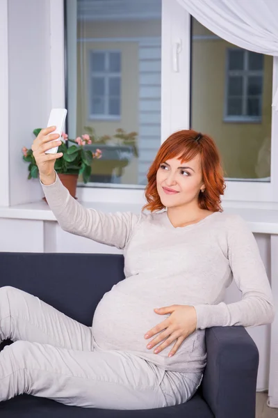 Joven embarazada tomando selfie foto con el teléfono inteligente en liv — Foto de Stock