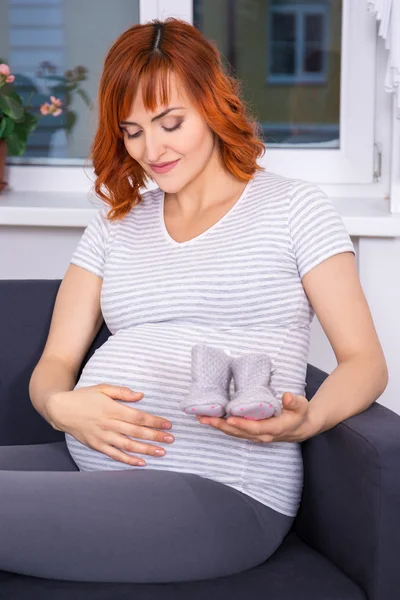 Mulher grávida sentada com peças de roupas para o bebê recém-nascido — Fotografia de Stock
