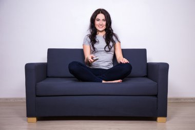 young woman sitting on sofa with remote control and watching tv 