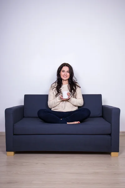 Young woman sitting on sofa with mug of tea at home — 스톡 사진