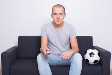 Futbol topu ile kanepede oturan ve evde tv izlerken bir adam
