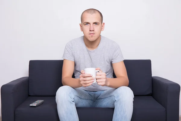 Portrait of handsome man sitting on sofa and watching tv with cu — Stock Photo, Image