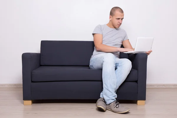 Homem bonito sentado no sofá e usando o computador — Fotografia de Stock