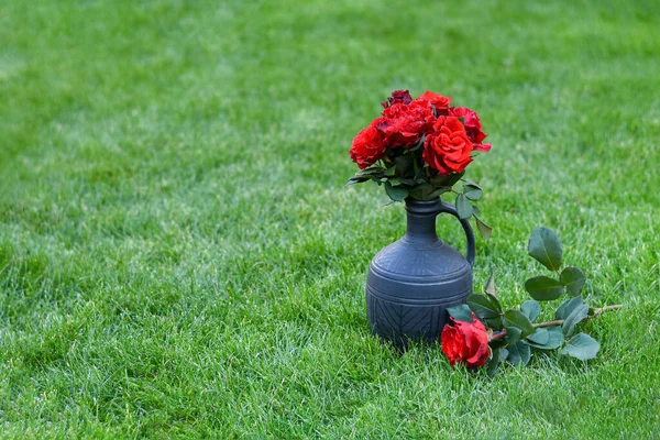 Bouquet de fleurs rouges dans un vase en argile sur une pelouse verte. Roses rouges sur un fond d'herbe verte. — Photo