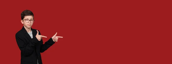 Cute boy with glasses, pointing his hands to empty place isolated on red, burgundy background. — Stock Photo, Image