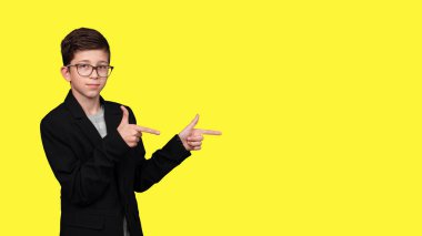 Gözlüklü sevimli çocuk, parlak sarı arka planda izole edilmiş boş bir yeri işaret ediyor..