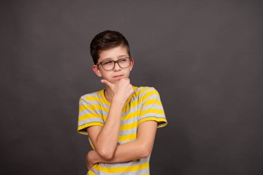 Gözlüklü çocuk. Düşünceli bir bakış. Koyu gri bir arkaplanda.