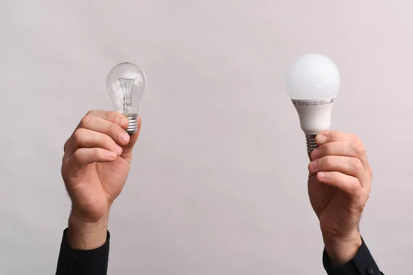 In the male hands, an LED lamp and an incandescent light bulb. The concept of energy saving.
