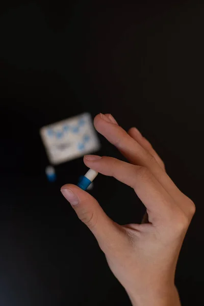 Main tenant une capsule pilule en gros plan sur un fond noir. — Photo