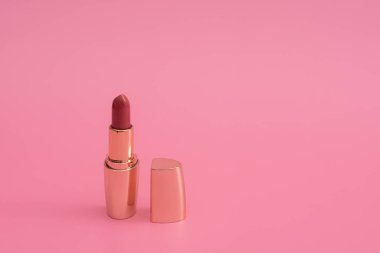 Altın kapaklı kırmızı ruj. Pembe bir arka planda. Boşluğu kopyala
