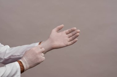 Doktor tek kullanımlık lastik koruyucu eldiven giyer. Gri arkaplanda yakın plan. 