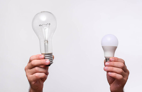 a large incandescent lamp and a small led lamp in the hands on a white background.