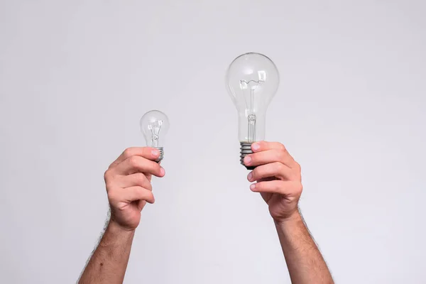 Dos bombillas en manos de hombre. lámparas incandescentes grandes y pequeñas. — Foto de Stock