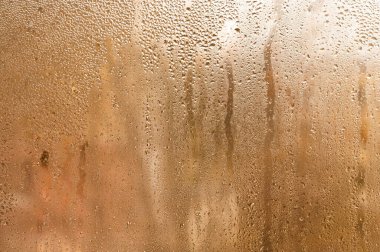 drops slowly sliding down wet window pane. Heavy condensation on apartment room window with thick water droplets obscuring view. brown backdoor. terracotta wet glass