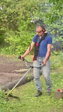 Adam arka bahçede benzin buduyor, fazla büyümüş çimleri kesiyor. Yeşil kırpıntılar yana doğru püskürtülmüş. Adam çimleri dikey tutmak için benzinle çalışan budayıcı kullanıyor.