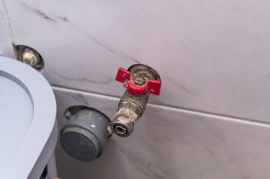 Banyo duvarında kırmızı saplı metal su vanası. Tesisat müfrezesi bakım, kontrol ve ev aletlerini sembolize ediyor. Tesisat musluğu ve filtre boru bağlantısının kapatılması