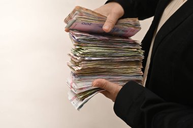 Uzun banknotlar, finansal büyüme ve kişisel zenginliğin sembolü ellerde. Kadın para yığını sunar, ekonomik başarıyı, karı ve gelir gücünü ifade eder. Ukrayna para birimi kadınların elinde.