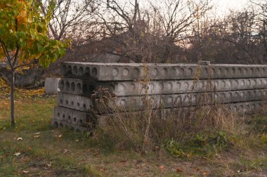 Endüstriyel açık alanda çimenlik alanda beton yığını. Bitkilerle çevrili açık havada depolanmış inşaat malzemeleri yığını..