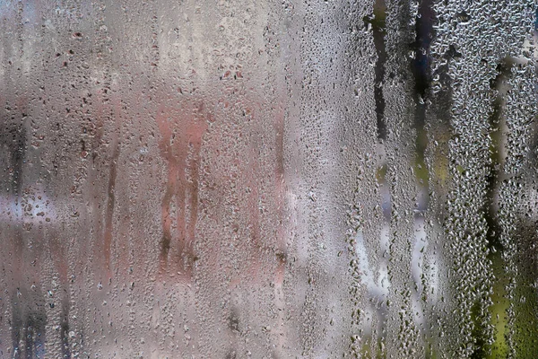 Su damlaları ıslak bir pencere camından akarak minimalist ve atmosferik bir zemin oluşturur. Damlacıkların doğal akışı. ıslak cam zemin.