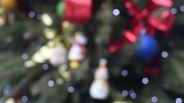 Noel ağacı ışıkları, bulanık, şenlikli bokeh atmosferde yavaşça parıldıyor. Renkli dekorasyonlar ve parıldayan ampuller nazikçe parıldıyor. Odaklanamayan Noel ışıkları bulanık ağaç dallarında güzel bir şekilde parlıyor..
