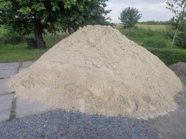 İnşaat alanındaki büyük kum yığını inşaat projelerinde kullanılmaya hazır. Kum düzgünce depolanmış. Yerdeki kum yığını, çakıl yolunun yanında.. 