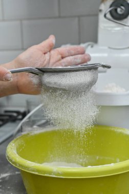 Sarı kase içine un elemek için elek kullanıyor. Ev yapımı pişirme işlemi malzeme hazırlığını, hamur yapımını sembolize eder. Un, elek eldiveni içinden geçiyor. dikey