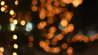 Sıcak altın bokeh ışıkları gece atmosferinde yavaşça hareket eder. Noel aydınlanması, ağaçların dallarında parıldayan sıcak tonlarla parlar. Parıldayan altın ışıklar koyu arkaplan üzerinde bohça deseni.