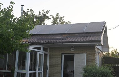 Çatı katında güneş panelleri olan, yeşilliklerle çevrili modern bir ev. Çevre dostu mimari ve sürdürülebilirlik vurgulanmıştır. Yenilenebilir enerji çözümleri. Güneş panelleri olan sürdürülebilir ev.