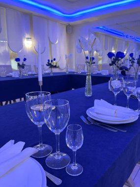 Şarap kadehleri, tabaklar ve düzgünce katlanmış peçetelerden oluşan zarif bir yemek masasının yakın çekimi. Bu çekimde masa düzeninin lüks atmosferi vurgulanıyor..