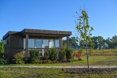 Kırsal kesimde geniş pencereli modern kulübe, çevre dostu ev tasarımı yeşil bitkiler ve açık alan ile çevrili, çağdaş mimari doğal ortam