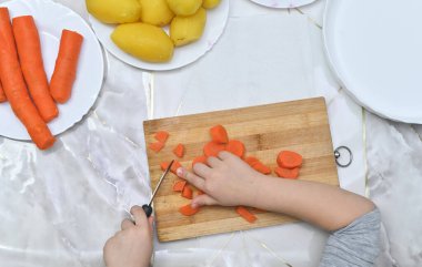 Anaokulu öğrencisi kaynamış havuç dilimleyerek yemek pişirmenin keyfini yaşıyor. Aile yemekleri ya da aşçı çocuk eğitimi için mükemmel bir fotoğraf. Kör bir güvenlik bıçağıyla sebzeleri dilimlemek.