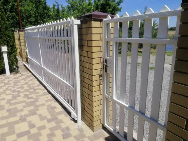 Özel evin girişinde tuğlalı sütunları olan beyaz sürgülü kapı modern açık hava tasarımı ve güvenliği sergiliyor. Çelik yapısı ve temiz çizgileri olan giriş kapısı. Kaleli kapı. konsept