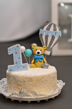 Doğum günü pastasının mavi ayı figürünün balon tutarken çekilmiş dikey fotoğrafı. Pasta, çocuklar için yapılan ilk doğum günü pastasıyla süslenir..