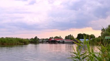 Deniz kenarındaki tekne rıhtımlarının manzarası. Sazlıklar kıyı şeridi boyunca büyürken sakin sular gökyüzünü yansıtarak tekne istasyonlarının etrafında barışçıl bir atmosfer yaratıyor..