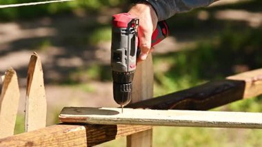 İnşaat sırasında ahşap tahtada matkap deliği. Kablosuz tornavida eylemi yakın plan, tahta tozu görünür, elektrikli alet kullanımı, açık hava el işçiliği kavramı