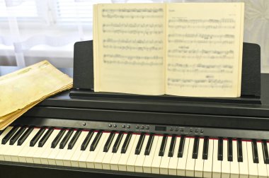 Elektronik piyanonun üzerinde duran müzik kitabı yaratıcılığı ve pratiği sembolize ediyor. notalar müzikal beceriler ve ilham için hayati bir araçtır..