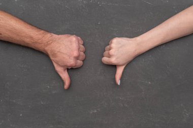 İki el, karanlık arka planda baş parmak hareketi gösteriyor. El işareti, hoşlanmadığını ya da reddedildiğini gösteriyor. Yakın çekim detayı, izole kompozisyon. Kadın ve erkek el hareketi reddediyor.