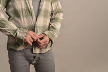 Giyinme rutini sırasında gömleği termal kıyafetin üstüne ilikleyen adam. Adam gömlek manşetlerini ve önünü sıcak taban tabakası, modern yaşam tarzı konsepti, tarafsız stüdyo arkaplanı, yakın çekim ayrıntıları giyerken ayarlar.