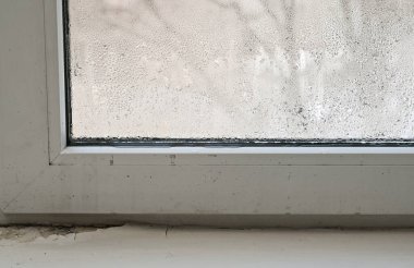 Pencere yüzeyini görünür damlacıklarla kaplayan yoğunlaşma. Çerçevenin kenarında nem birikiyor. Yakın çekim nem oranı. Soğuk mevsim atmosferi, içerideki rutubet sorunu. Yüksek nemli mikroiklim odası.