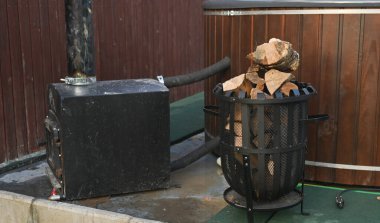 Metal odun sobası ve ahşap fıçının yanında bacası olan açık hava jakuzisi çitin yanındaki verandaya kurulmuş. Yakacak odunla ısıtılan jakuzi banyo ve rahatlama için, sağlık konsepti, arka bahçe.