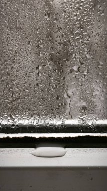 Pencere camını kaplayan buhar damlaları, soğuk yüzeyde dikey akıntılar oluşturan nem boncukları. Yoğunlaştırılmış doku karamsar yağmurlu atmosfer, detay, yakın plan, hava konsepti