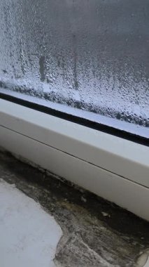 İçerideki dairenin penceresi yüksek yoğunluk nedeniyle su damlacıklarıyla kaplı. dikey video. Damlalar ve sis camları. Hafif bir su birikintisi. ıslak pencere camı. Nem pervazı çöker..