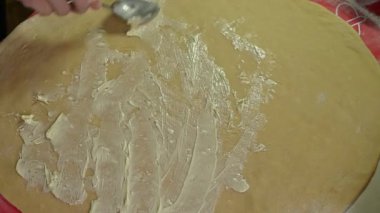 Elleri bir kaşık kullanarak hamurun üzerine tereyağı serpiştirip, taze ev yapımı hamur işi veya ekmek yapmak için bir sonraki aşamaya hazırlıyor..