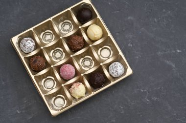 Çikolata şekerlemeleri açık altın kutunun içinde, arka planda koyu renkli, tepeden görülebiliyor. Farklı dolgulara sahip çikolata çeşitleri ve bitirmeler düzgün bir ızgara oluşturuyor. Hediye konsepti, tatlı çeşidi, tatlı,