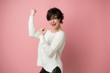 Beautiful young woman happy and excited expressing winning gesture. Successful and celebrating victory, triumphant, studio shot over pink background clipart